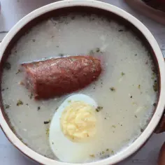 Aromaticzny żurek z kiełbasą i jajkiem, przygotowany na bazie domowego zakwasu na żurek. Obok czosnek, cebula i jajka.