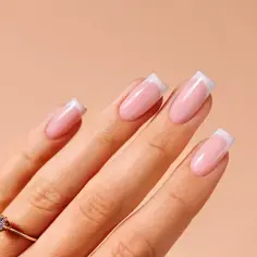 Dłoń z idealnym **manicurem francuskim**. Paznokcie w delikatnym różu z białymi końcówkami, ozdobione subtelnym pierścionkiem z brylantem.