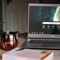 Acer Chromebook na drewnianym blacie, obok miedzianego kubka i światełek. To idealne urządzenie, jeśli zastanawiasz się, chromebook co to.