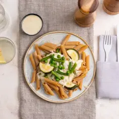Makaron pełnoziarnisty penne z warzywami i kremowym sosem na talerzu.