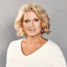 Uśmiechnięta Ewa Kasprzyk w białym swetrze. Wiele osób zastanawia się, ile lat ma Ewa Kasprzyk, ale jej wiek nie wpływa na jej energię.
