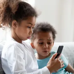 Dzieci próbują dowiedzieć się, jak usunąć kontrolę rodzicielską Family Link z telefonu dziecka, patrząc na ekran.