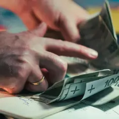 Dłonie liczą banknoty 100 zł. Zastanawiamy się, ile wynosi średnia krajowa, analizując wydatki.