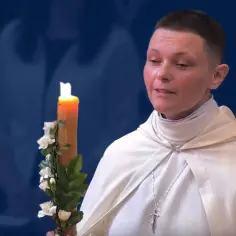 Kobieta w białej szacie trzyma ozdobioną świecę.