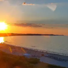 Zachód słońca nad Bałtykiem w Świnoujściu. Słońce odbija się w wodzie, a plaża tętni życiem.