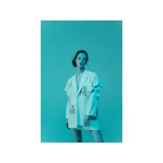 Modelka w białej, ozdobnej marynarce na turkusowym tle.