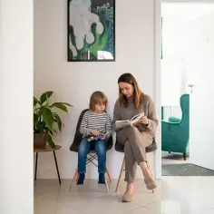 Kobieta czyta książkę, siedząc obok dziecka bawiącego się klockami w poczekalni.