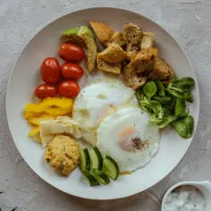 Talerz z jajkami sadzonymi, pomidorkami, awokado, grzankami i warzywami. Idealny posiłek na śniadanie, wspierający dietę jajeczną.