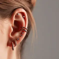 Ucho ozdobione wieloma kolczykami do piercingu ucha: kółka, kulki i ozdoby z cyrkoniami.