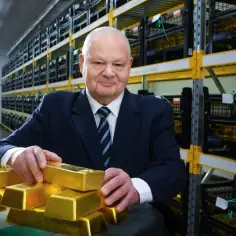 Mężczyzna w garniturze w magazynie Narodowego Banku Polskiego, trzymający sztabki złota. Pokazuje, ile złota ma Polska.