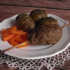 Kebab z mielonego na patyku z pieczonymi ziemniakami i marchewką na talerzu.