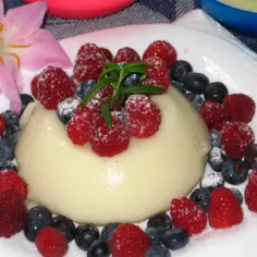 Panna cotta z malinami i borówkami, posypana cukrem pudrem. Idealny deser, który możesz przygotować według prostego legumina przepis.