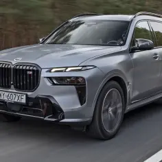 Szary BMW X7 2025 z czarnym grillem i sportowymi akcentami pędzi po drodze.