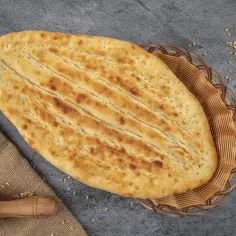 Chlebek naan w koszyku, obok wałek i ziarna pszenicy.