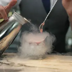 Barman tworzy efektowny dym w drinku, używając metalowego dzbanka i łyżki. To sposób, jak zrobić efektowny dym w drinku bez użycia suchego lodu.