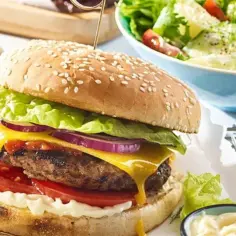 Soczysty burger z grilla z topniejącym serem, chrupiącą sałatą, pomidorem i czerwoną cebulą, podany z sałatką ziemniaczaną.