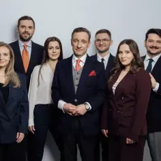 Grupa prawników w garniturach pozuje do zdjęcia na jasnym tle.