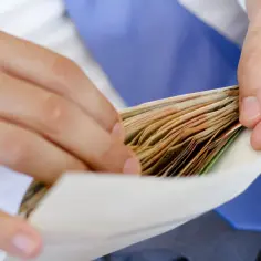 Dłonie wkładają plik banknotów do koperty. Zastanawiam się, ile na wesele od chrzestnej.