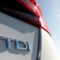 Błyszczące logo TDI na białym samochodzie pod błękitnym niebem. To oznaczenie silnika, co to znaczy?