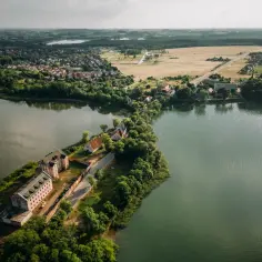 Ruiny zamku w Ełku na wyspie, otoczone zielenią i wodą. W tle widać miasto i jeziora.
