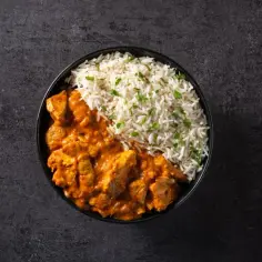 Aromaticzny kurczak po indyjsku w kremowym sosie, podany z ryżem basmati i posypany świeżą kolendrą.