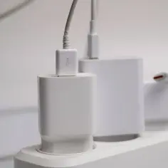 Białe ładowarki podłączone do listwy zasilającej. Na jednym z kabli widnieje symbol USB, który pomaga określić, który kabel to plus, a który minus w ładowarce.