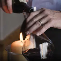 Mężczyzna dekantuje czerwone wino nad płonącą świecą do karafki.