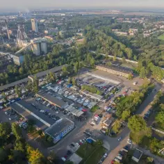 Tętniący życiem targ samochodowy, gdzie można sprawdzić, czy giełda samochodowa jest czynna w niedziele, otoczony zielenią i przemysłowymi budynkami.