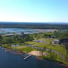Malownicze **Mazury Garbate** z lotu ptaka: jezioro, plaża, hotel i stawy hodowlane.