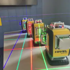 Kilka poziomnic laserowych emitujących zielone, czerwone i niebieskie linie na białej powierzchni.