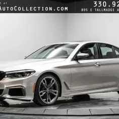 Srebrny sedan BMW m550i z czarną atrapą chłodnicy i felgami stoi na obrotowej platformie.