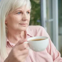 Blondynka z niebieskimi oczami popija kawę na czczo, patrząc w dal.