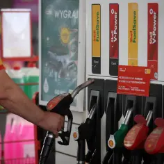 Ręka trzymająca dystrybutor paliwa na stacji Shell. Promocja "Przetestuj paliwa premium w cenie paliw podstawowych" sugeruje, ile można zarobić na stacji benzynowej, oferując lepsze paliwo w niższej cenie.