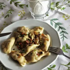 Pyszne pierogi ruskie z farszem Magdy Gessler, polane skwarkami i szczypiorkiem, na obrusie w zielone listki.