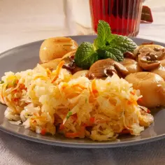 Na talerzu aromatyczna surówka z kiszonej kapusty, obok pieczone ziemniaczki i grzyby, udekorowane listkiem mięty.