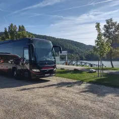 Czarny autokar Eurotrans czeka nad rzeką. Zastanawiasz się, ile się jedzie autokarem do Grecji?
