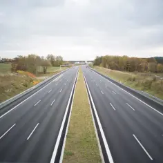 Pusta autostrada w Niemczech, z pasem zieleni pośrodku. W oddali widać budynki i jesienne drzewa.