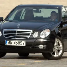 Czarny Mercedes w211 z kierowcą za kierownicą, zaparkowany na zewnątrz.