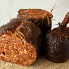Trzy kawałki kalabryjskiej kiełbasy nduja, zawinięte w brązowy papier, na desce.