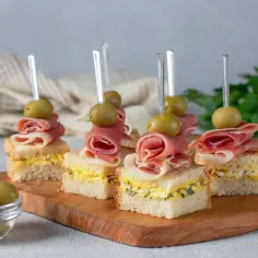 Mini kanapki z szynką, jajkiem i oliwkami na drewnianej desce. Idealne na grilla tanio i elegancko.