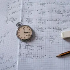 Zegar kieszonkowy obok zeszytu z zadaniami z matematyki. Ile trwa rozszerzenie z biologii? Czas ucieka!
