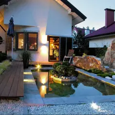 Oświetlenie zewnętrzne domu jednorodzinnego tworzy magiczną atmosferę wokół oczka wodnego i skalnych formacji.