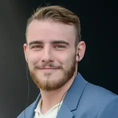 Krystian Ochman w niebieskiej marynarce, z zarostem i słuchawkami w uszach. Może właśnie rozmawia ze swoją żoną przez telefon.