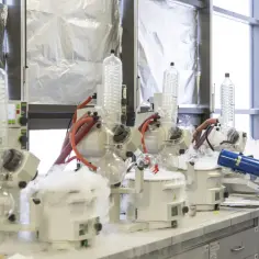 Naukowczyni w laboratorium z aparaturą do destylacji. Dymiące urządzenia symbolizują uniwersalizm nauki, która przekracza granice.