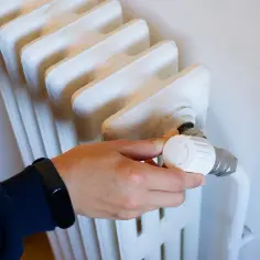 Dłoń kręci termostatem grzejnika, próbując rozwiązać problem, że najdalszy grzejnik nie grzeje.