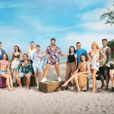Grupa młodych ludzi na plaży, gotowa na przygodę. Trzymają walizki, a ich stroje sugerują wakacyjny klimat. good luck guys!