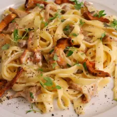 Pyszny makaron tagliatelle w kremowym sosie kurkowym, posypany świeżymi ziołami i pieprzem.