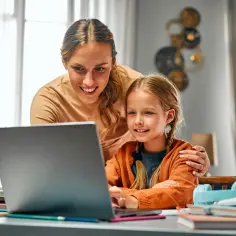Mama i córka korzystają z laptopa podczas urlopu. Opieka nad dzieckiem w domu to też nauka i zabawa.