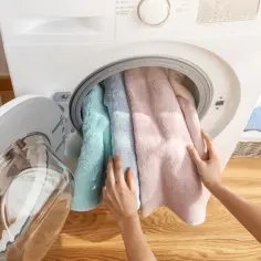 Ręce wkładają kolorowe ręczniki do pralki.