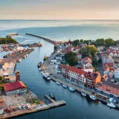 Widok z lotu ptaka na port i miasteczko, gdzie leży Ustka. Widać łodzie, budynki i morze.